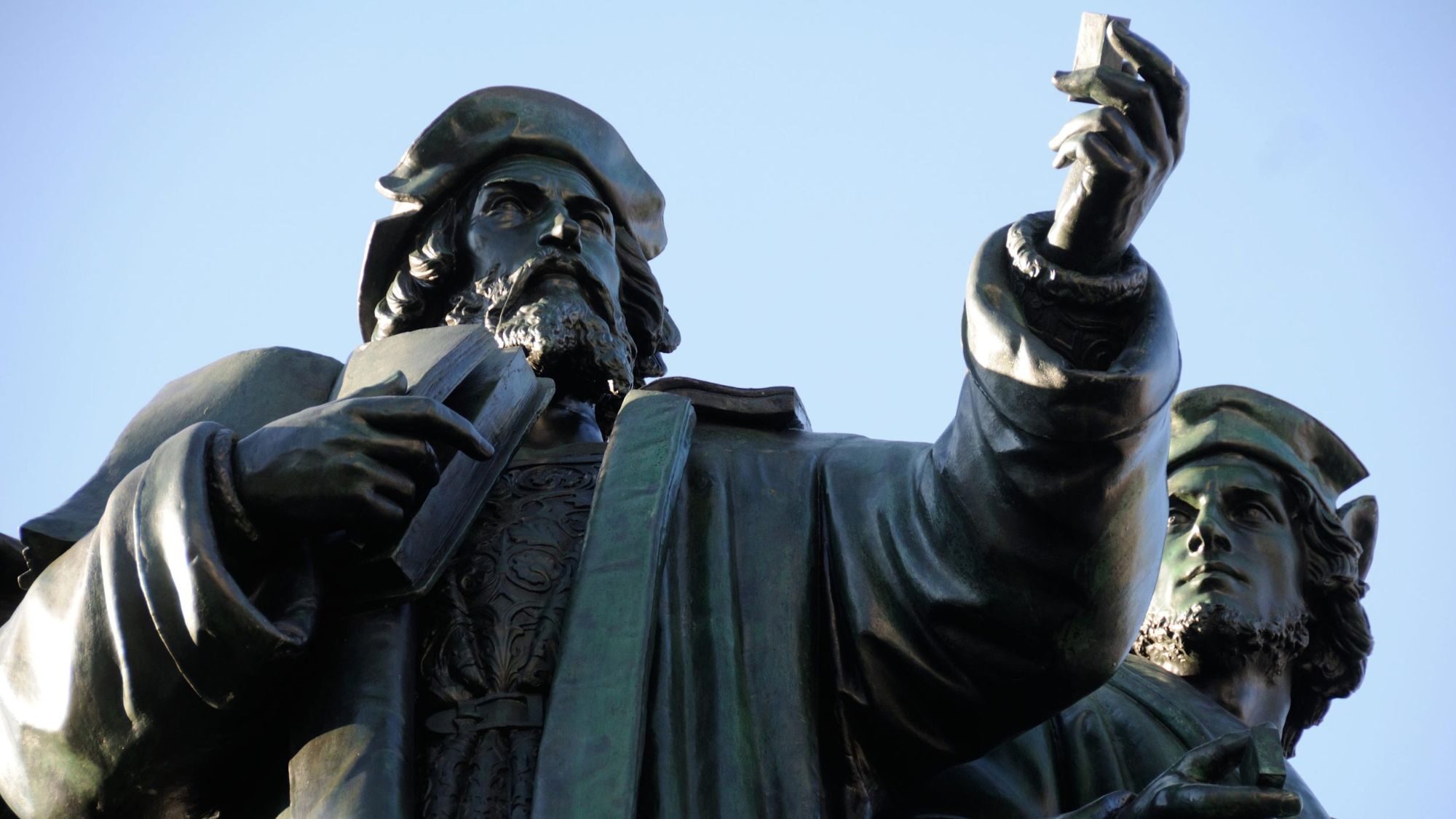 Bronze statue of Johannes Gutenberg holding up a piece of movable type, with a second printer behind him.