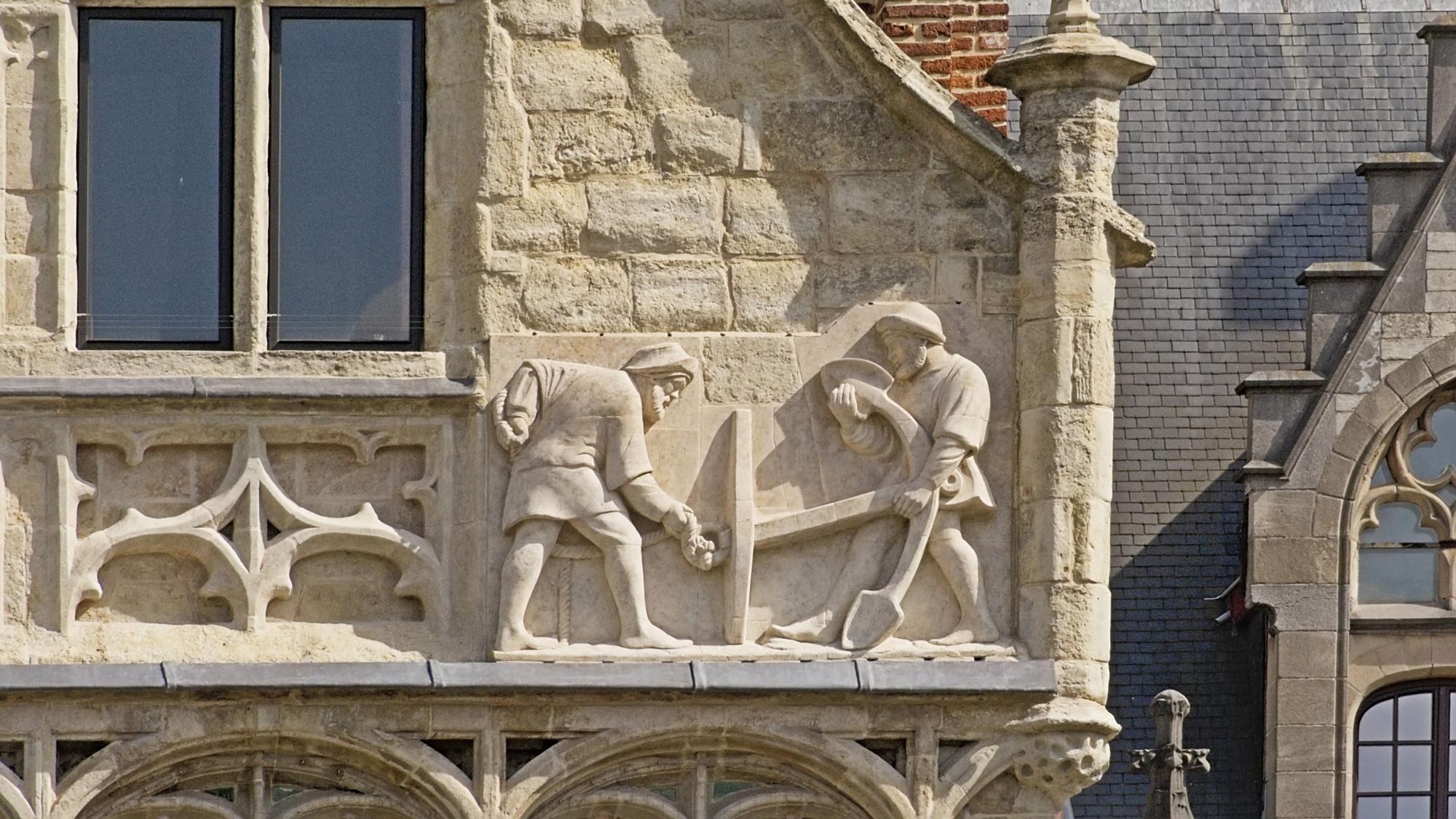 Stone relief of two craftsmen at work on the facade of a medieval guild house in Ghent.