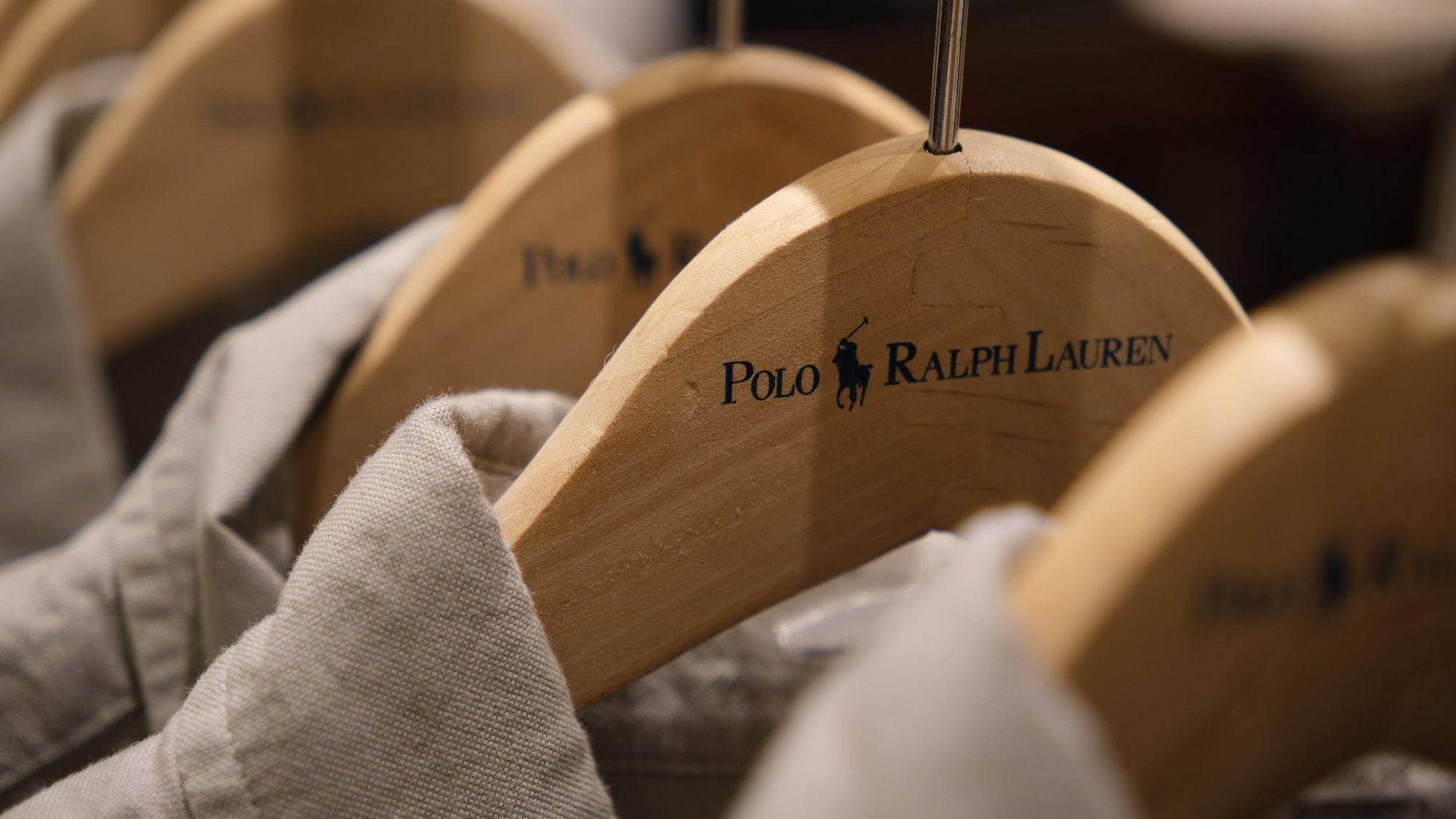 Wooden clothes hangers printed with the Polo Ralph Lauren logo, holding linen shirts on a rail.